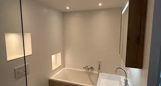 Badkamer met ligbad, hangtoilet, wastafelmeubel en glazen douchewand