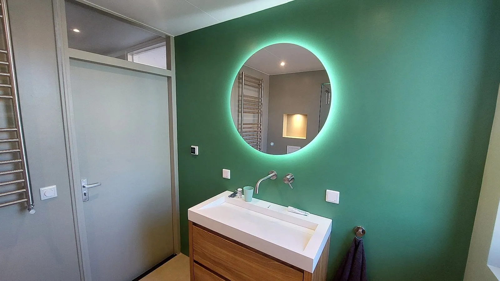 Groene wand met verlichte ronde spiegel na de renovatie — badkamerrenovatie in Sauwerd door BontBouw