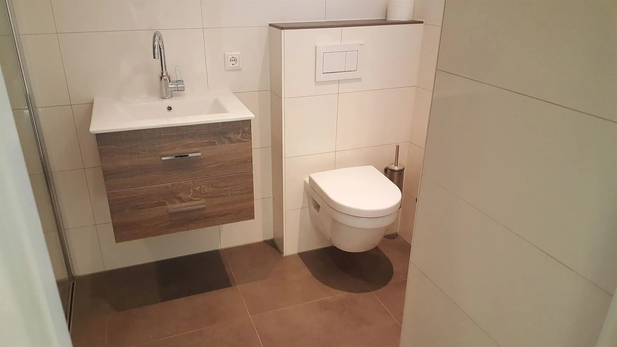 Hangtoilet en houten wastafelmeubel met bruine vloertegels na de renovatie — badkamerrenovatie in Peize door Bontbouw
