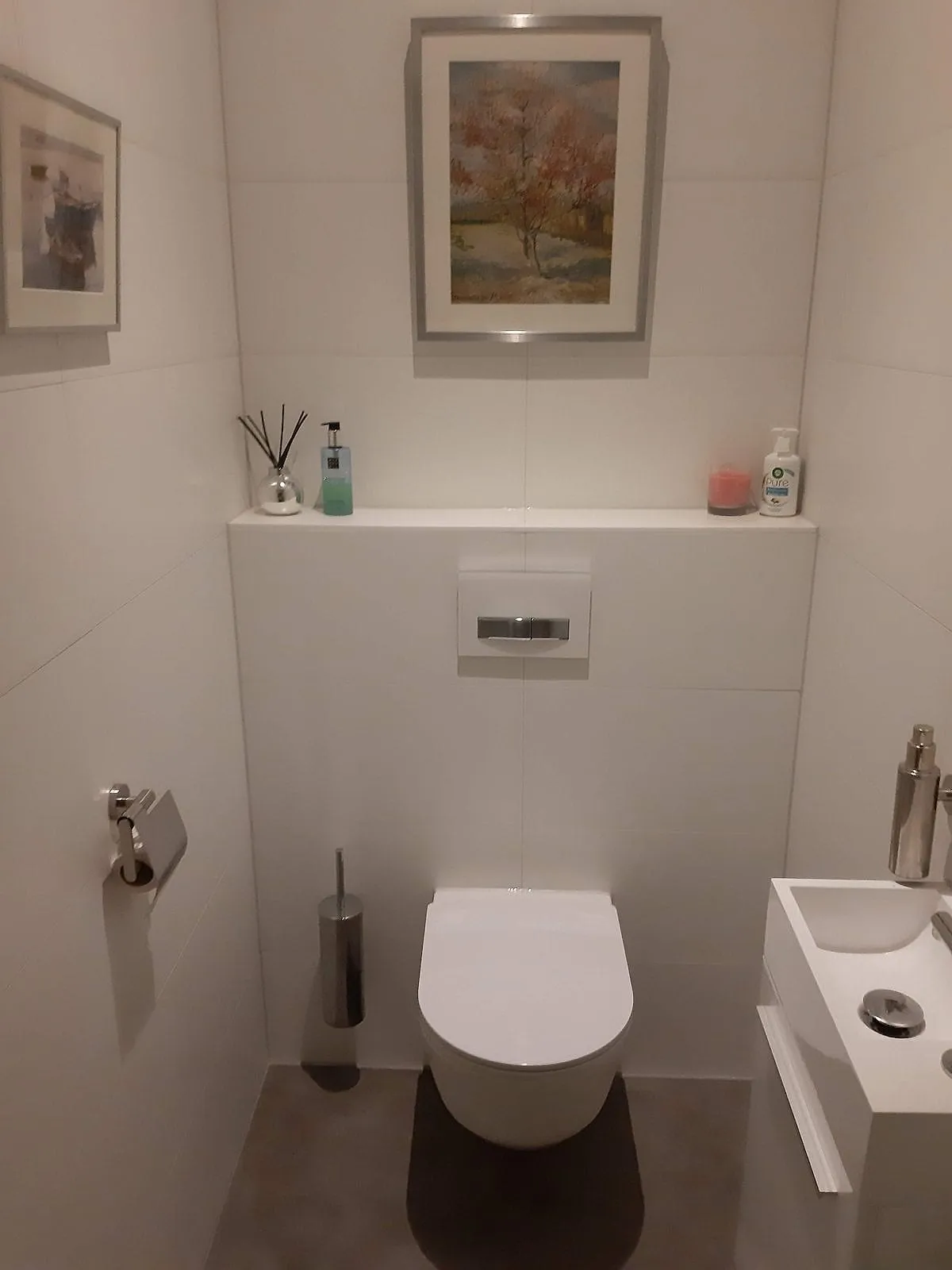 Hangtoilet met witte wandtegels en tegelrichel met schilderij na de renovatie — toiletrenovatie in Herewegbuurt door BontBouw