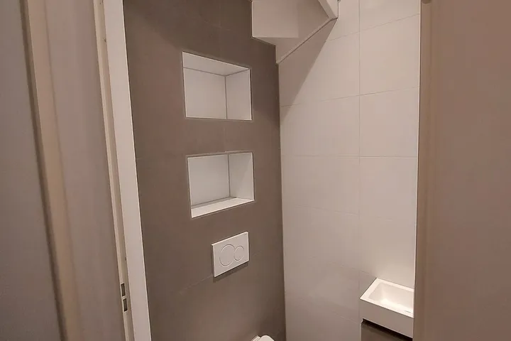 Hangtoilet onder de trap met taupe tegelwand en twee nissen in Schildersbuurt