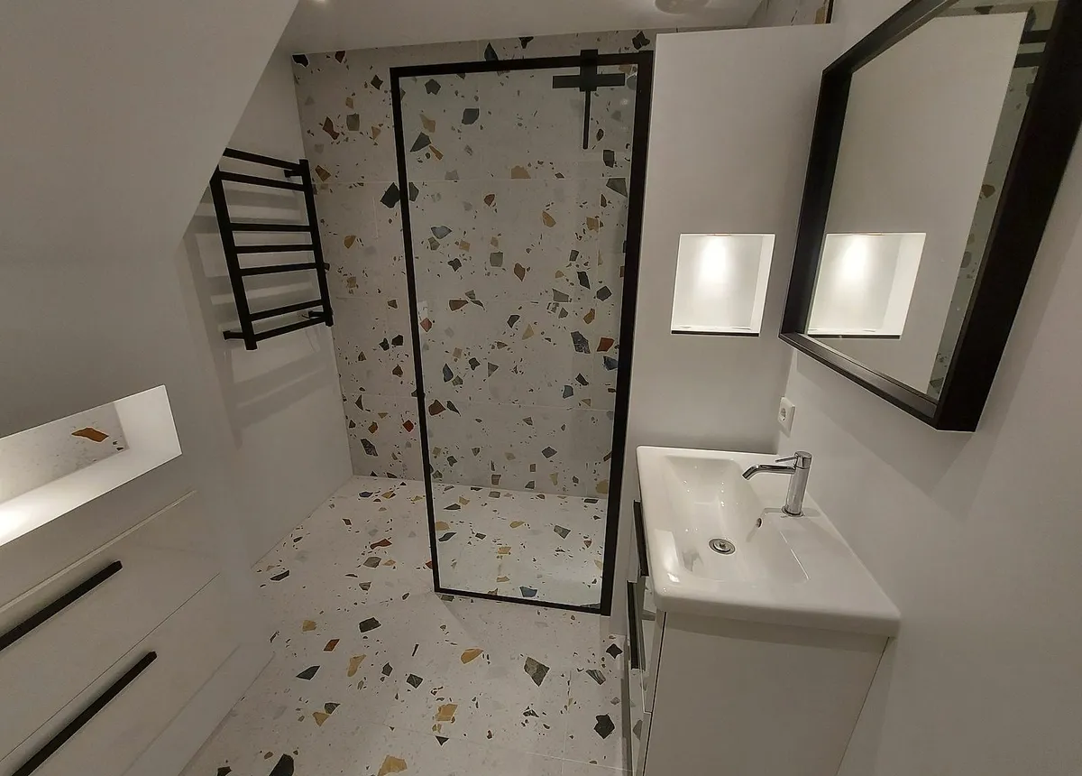 Inloopdouche met een zwart omlijnde glazen wand in een kleine badkamer onder een schuin dak in de Schildersbuurt