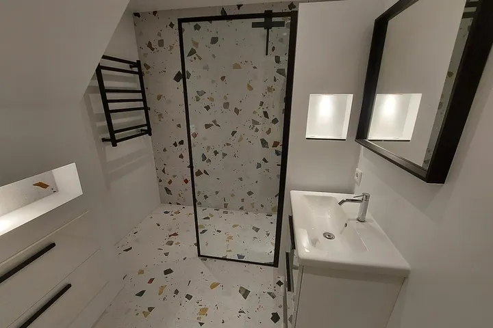 Inloopdouche met een zwart omlijnde glazen wand in een kleine badkamer onder een schuin dak in de Schildersbuurt