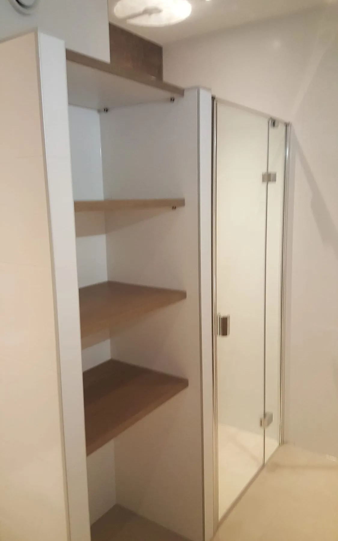Open kast met houten schappen naast de glazen douchedeur na de renovatie — badkamerrenovatie in Hoogezand door BontBouw